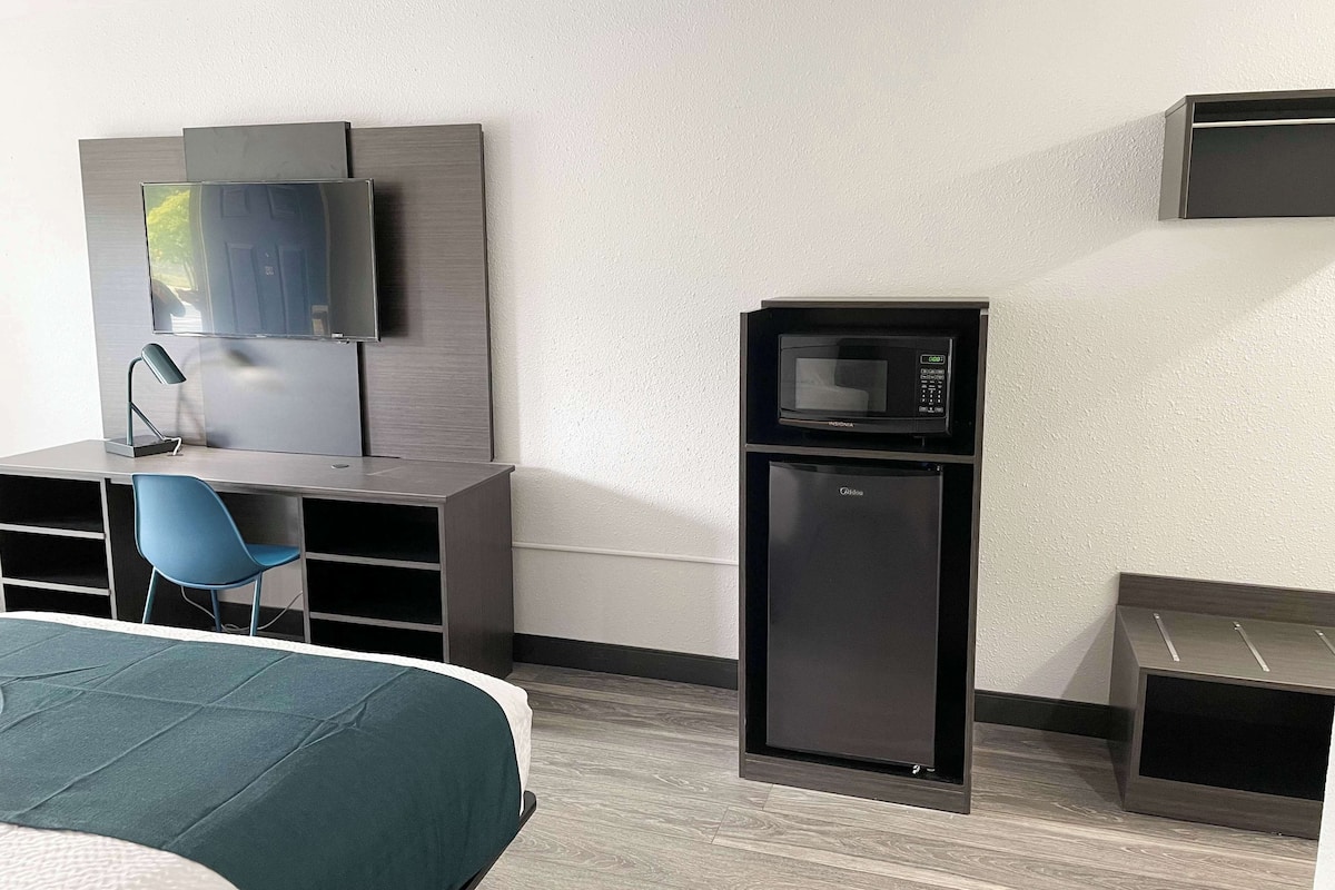 Hotelkamer met een bed, een bureau met stoel, een televisie, een magnetron en een kleine koelkast.