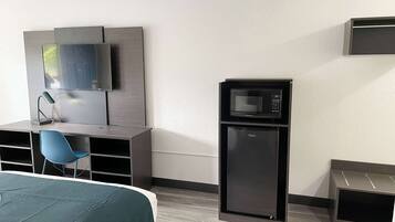 Habitación de hotel con cama, escritorio con silla, televisor, microondas y refrigerador pequeño.