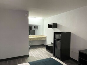A compact hotel room with a bed, a small kitchenette, a microwave, and a mirror. - Motel 6 West Columbia, SC - Airport (West Columbia)