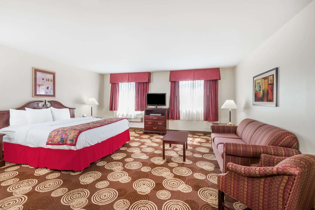 A hotel room with a large bed, a sofa, a TV, and a desk.
