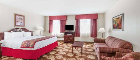 A hotel room with a large bed, a sofa, a TV, and a desk.