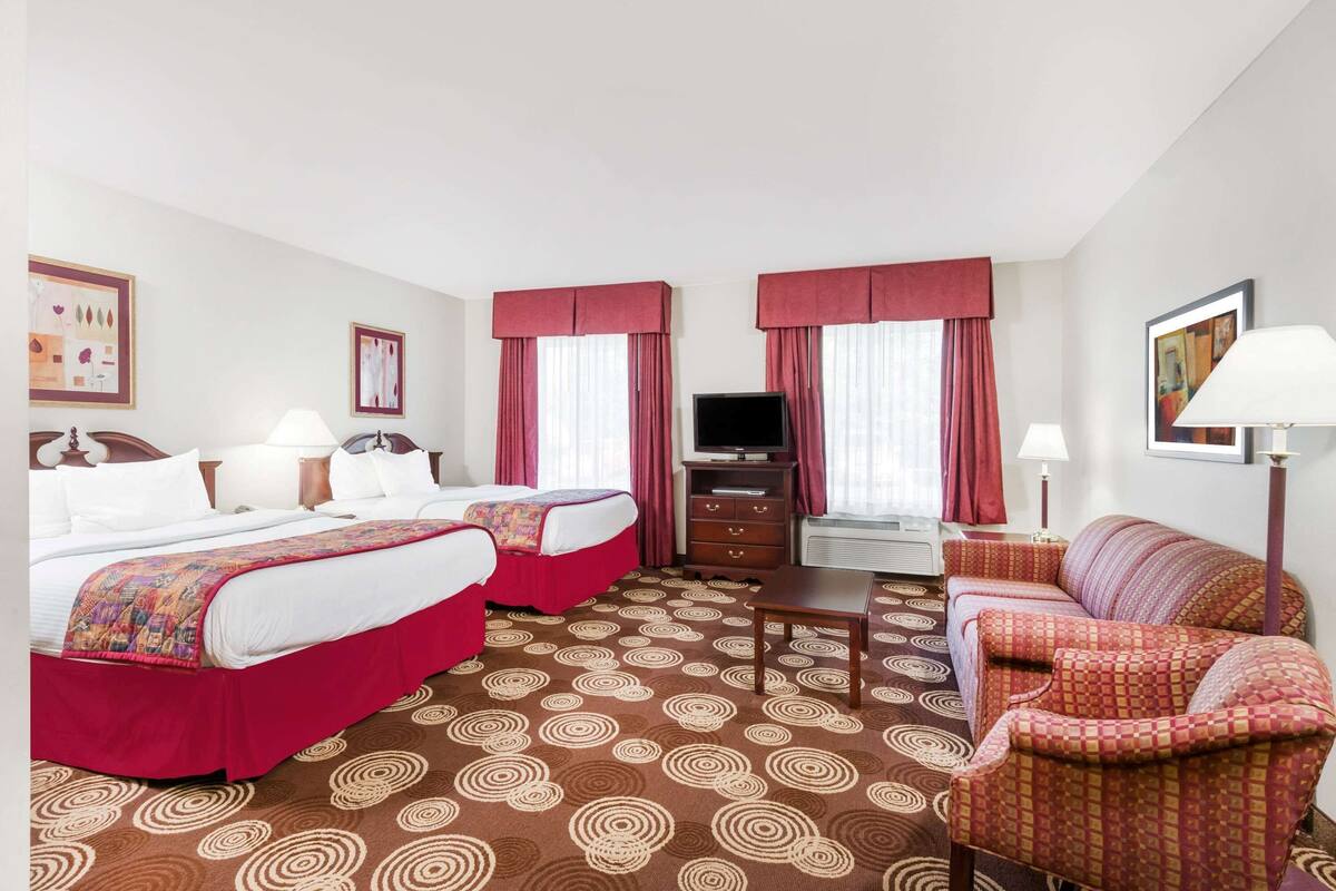 A hotel room with two beds, a TV, a desk, and a sofa.