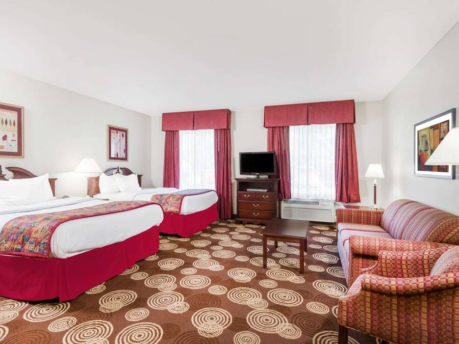 A hotel room with two beds, a TV, a desk, and a sofa.