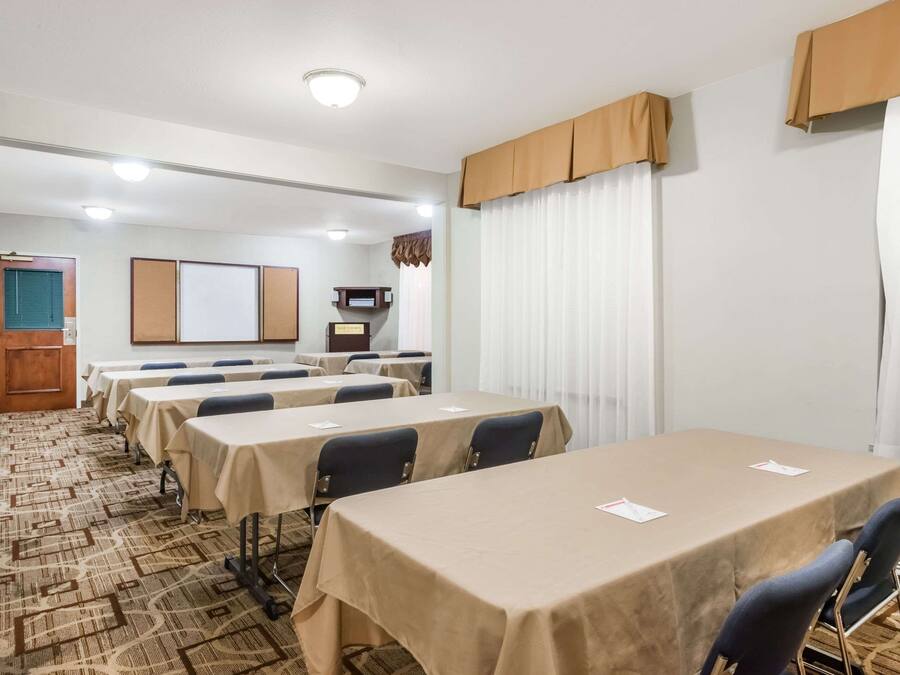 Un salón de conferencias con varias mesas, sillas, una pantalla de proyector y una pizarra.