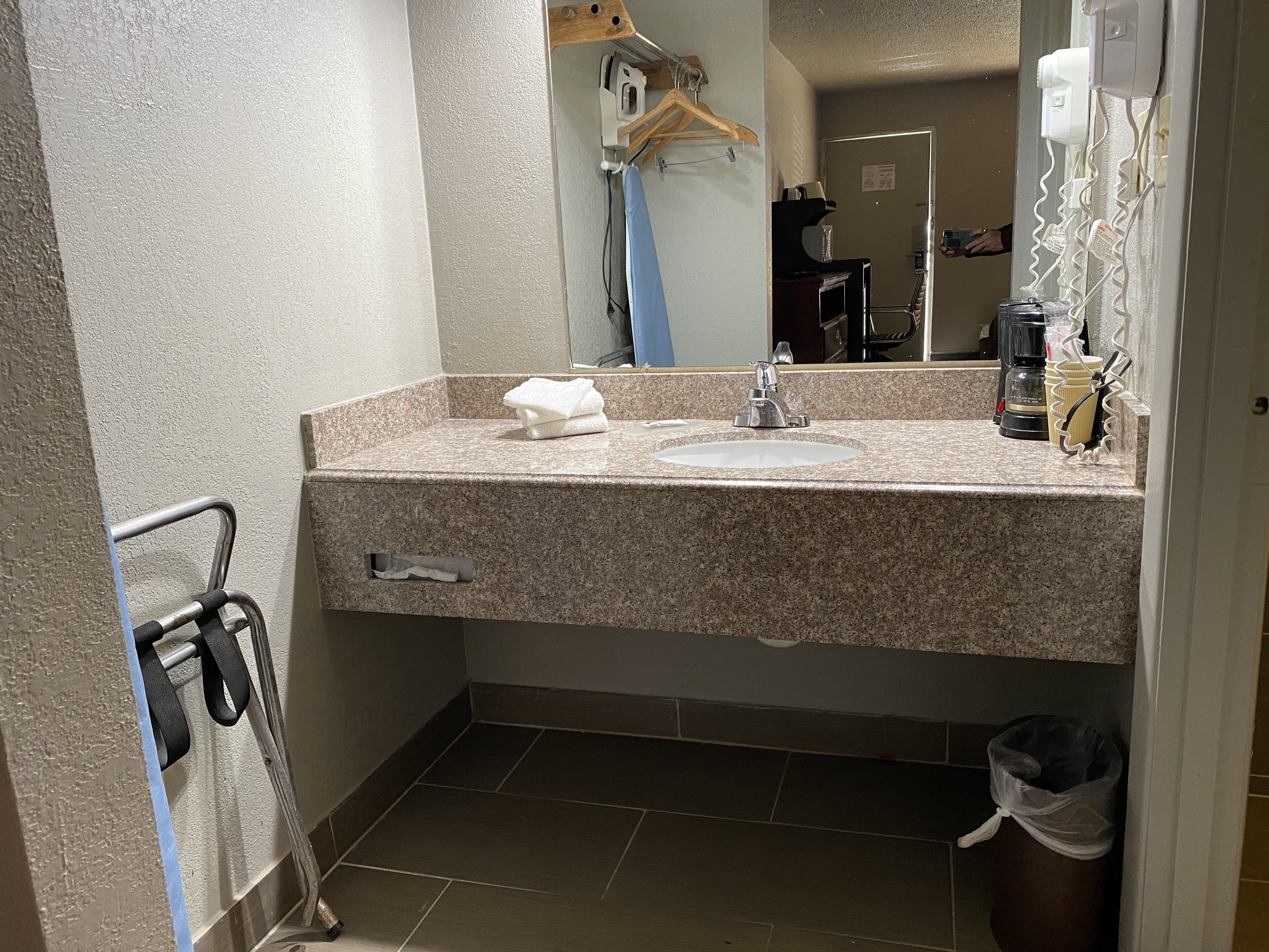 Een badkamer met een granieten aanrecht, een wastafel, een spiegel, een handdoekhouder en een prullenbak.