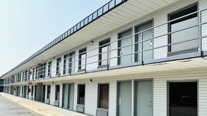 A row of single-story motel rooms with individual entrances and a parking lot in front. - Rogers Inn (Rogers)