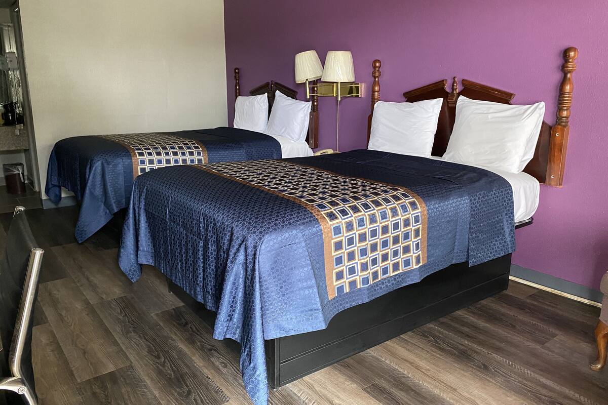 Quarto de hotel com duas camas, cada uma com cabeceira de madeira e colcha estampada.