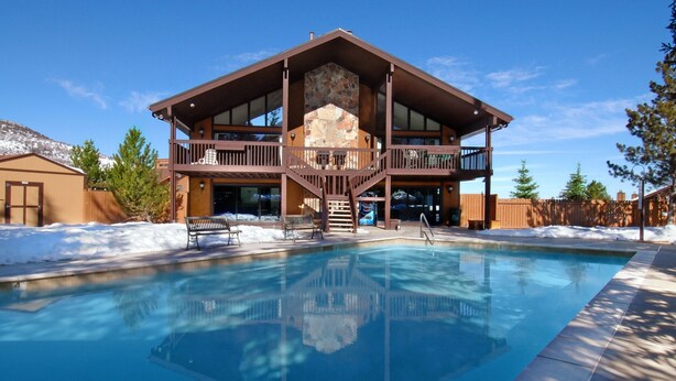 A two-story lodge with a stone fireplace, a pool, and a deck with benches. - Red Pine Condominiums by All Seasons Resort Lodging (Park City)