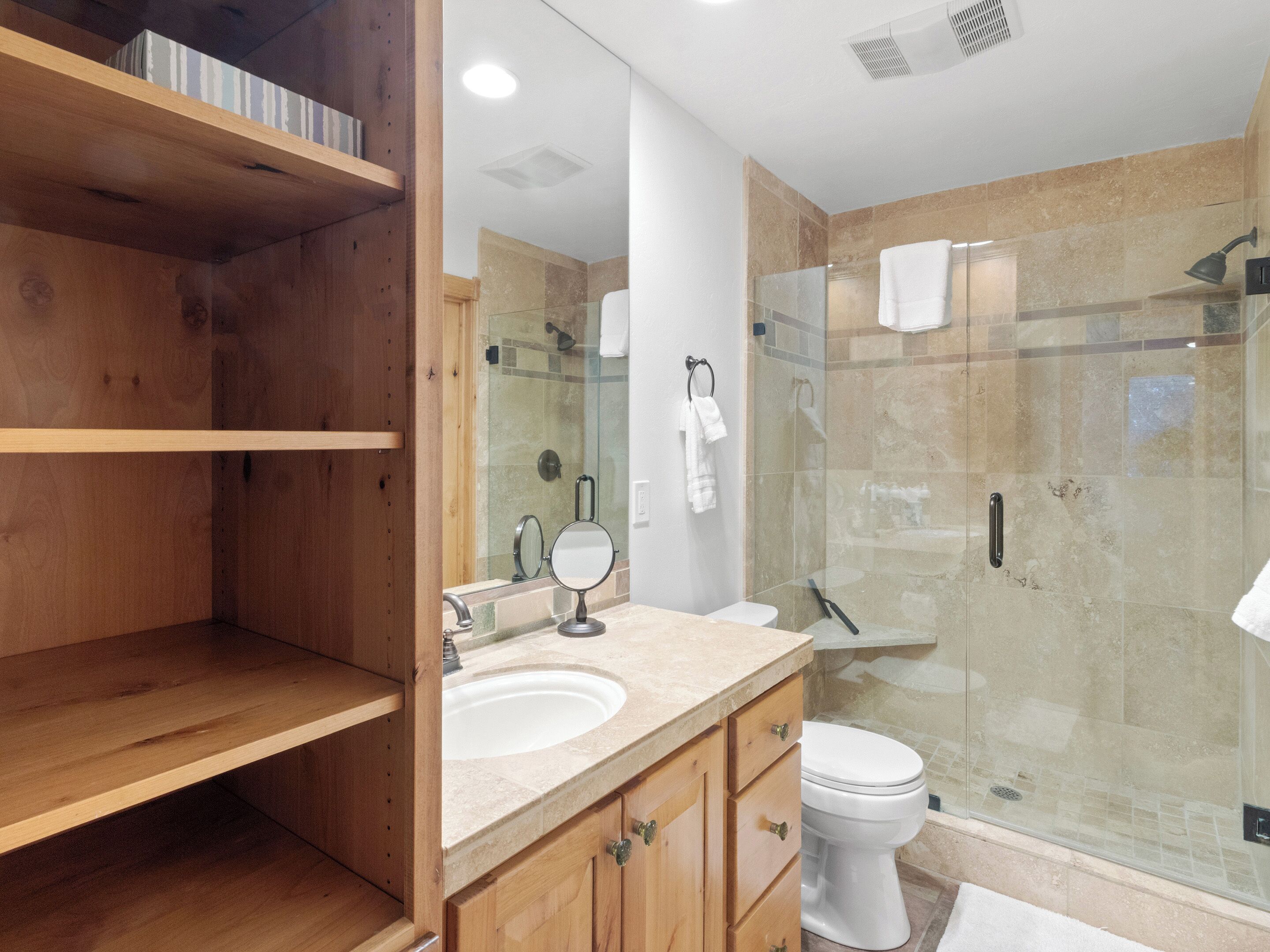 Ein modernes Badezimmer mit Holzausstattung, einer Glaskabine für die Dusche und einem weißen Waschbecken.