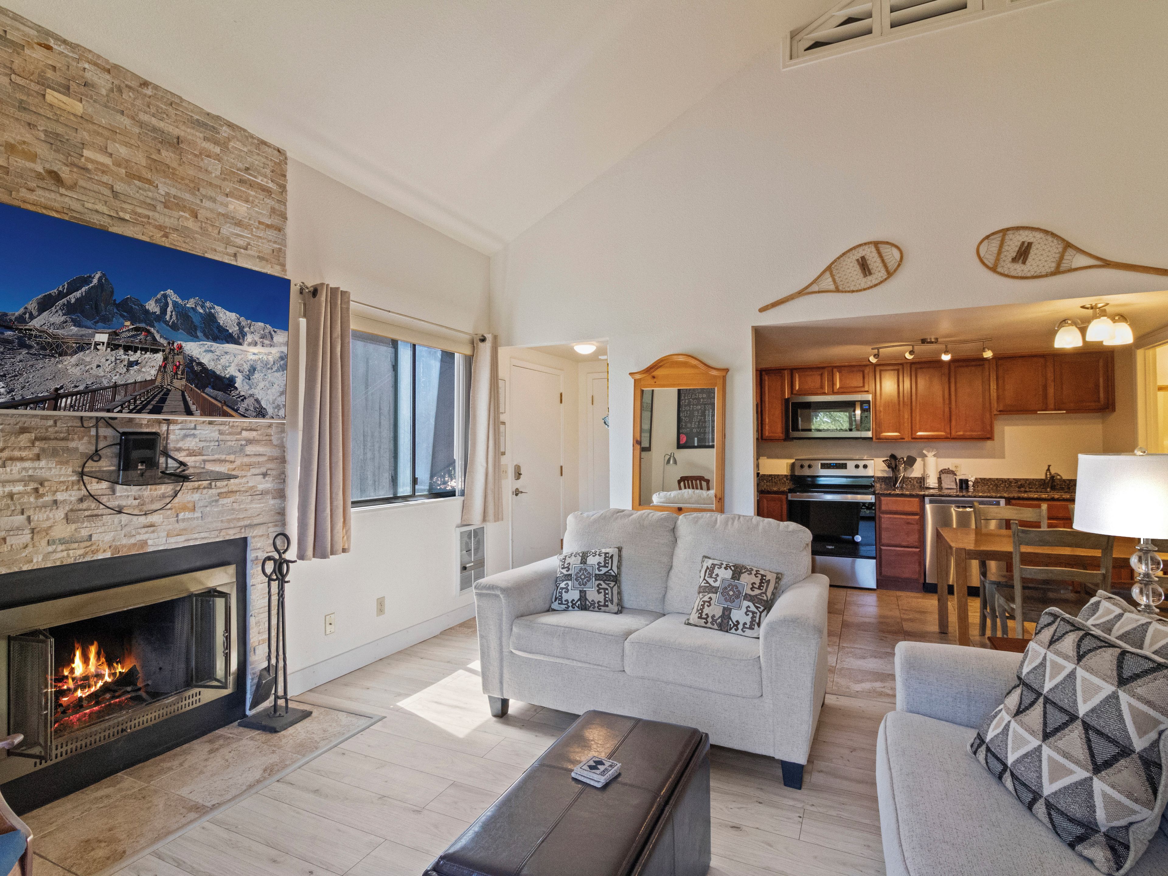 A living room with a fireplace, a sofa set, and a kitchen area with wooden cabinets and a microwave.