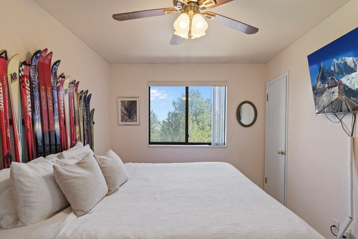 Une chambre à coucher avec un lit, un ventilateur de plafond, une fenêtre donnant sur des arbres et un mur décoré de paires de skis.