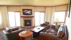 A hotel room with a fireplace, a television, leather sofas, and a patterned carpet.