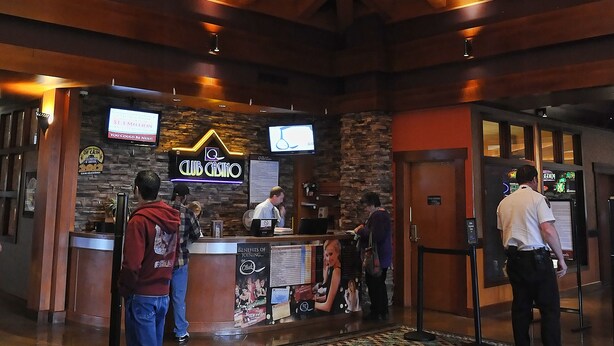 A lobby with a wooden ceiling and a patterned carpet. There is a reception desk with a neon sign and a television.