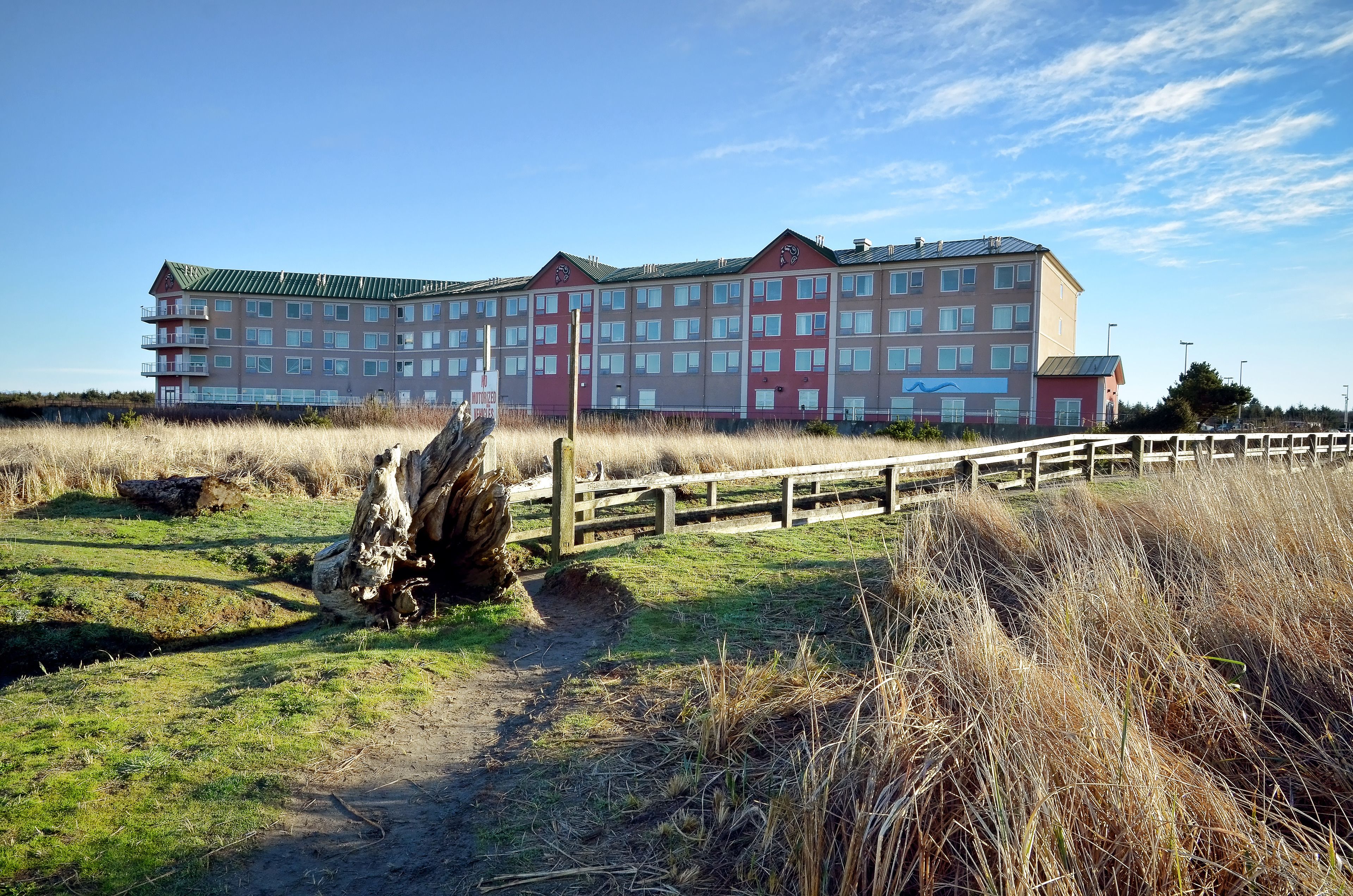 A multi-story hotel with a green roof, surrounded by grassy fields and a wooden fence.