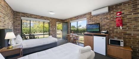 A hotel room with two beds, a television, a small refrigerator, and a window overlooking a garden.