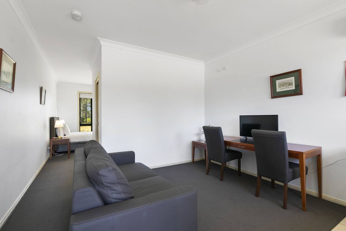 A modern room with a grey sofa, a wooden desk with a chair, a television, and a small table with a lamp.