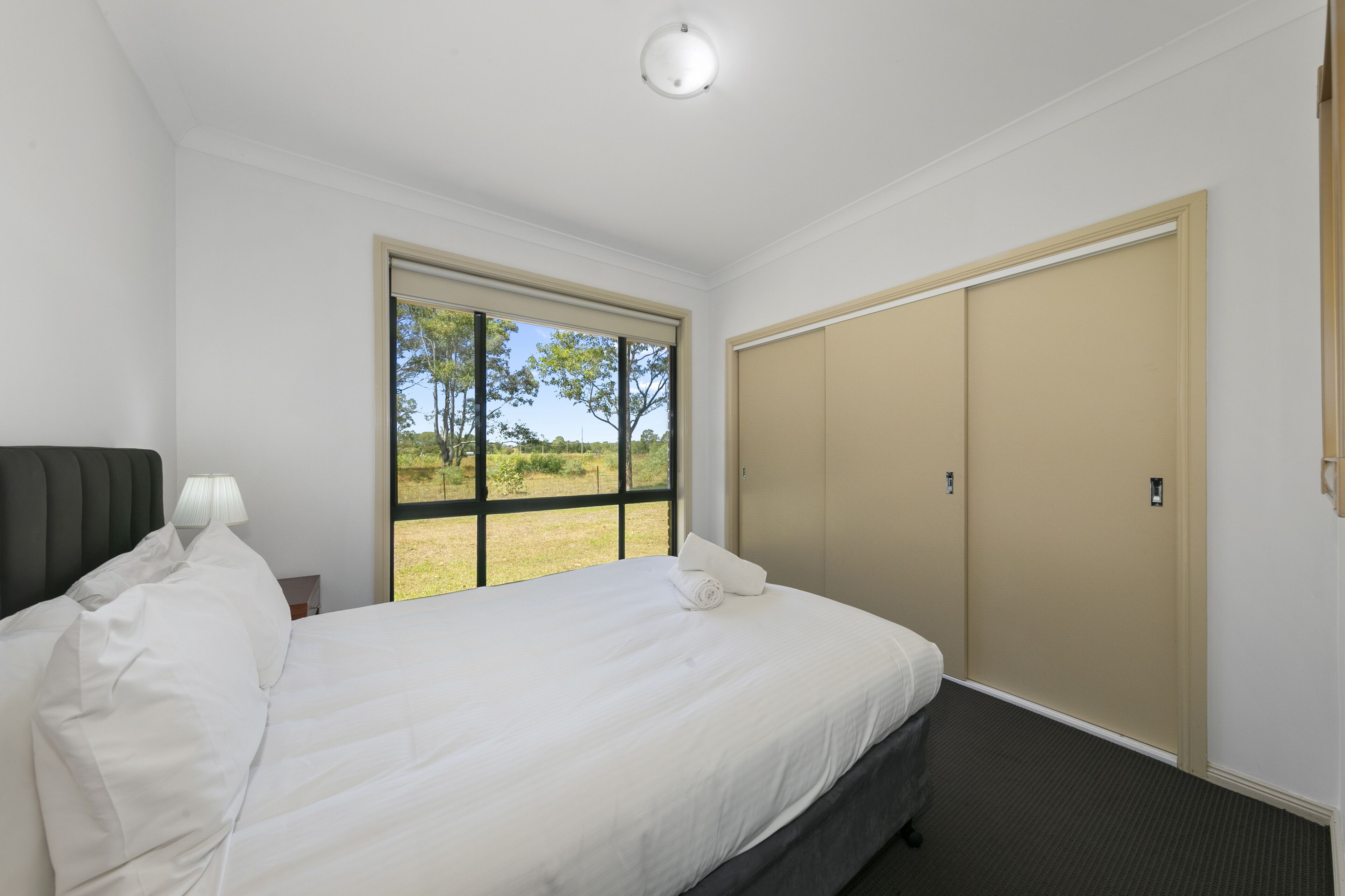 Ein Hotelzimmer mit Bett, Nachttisch, Lampe, Fenster mit Blick auf Grünflächen und einem Schrank.