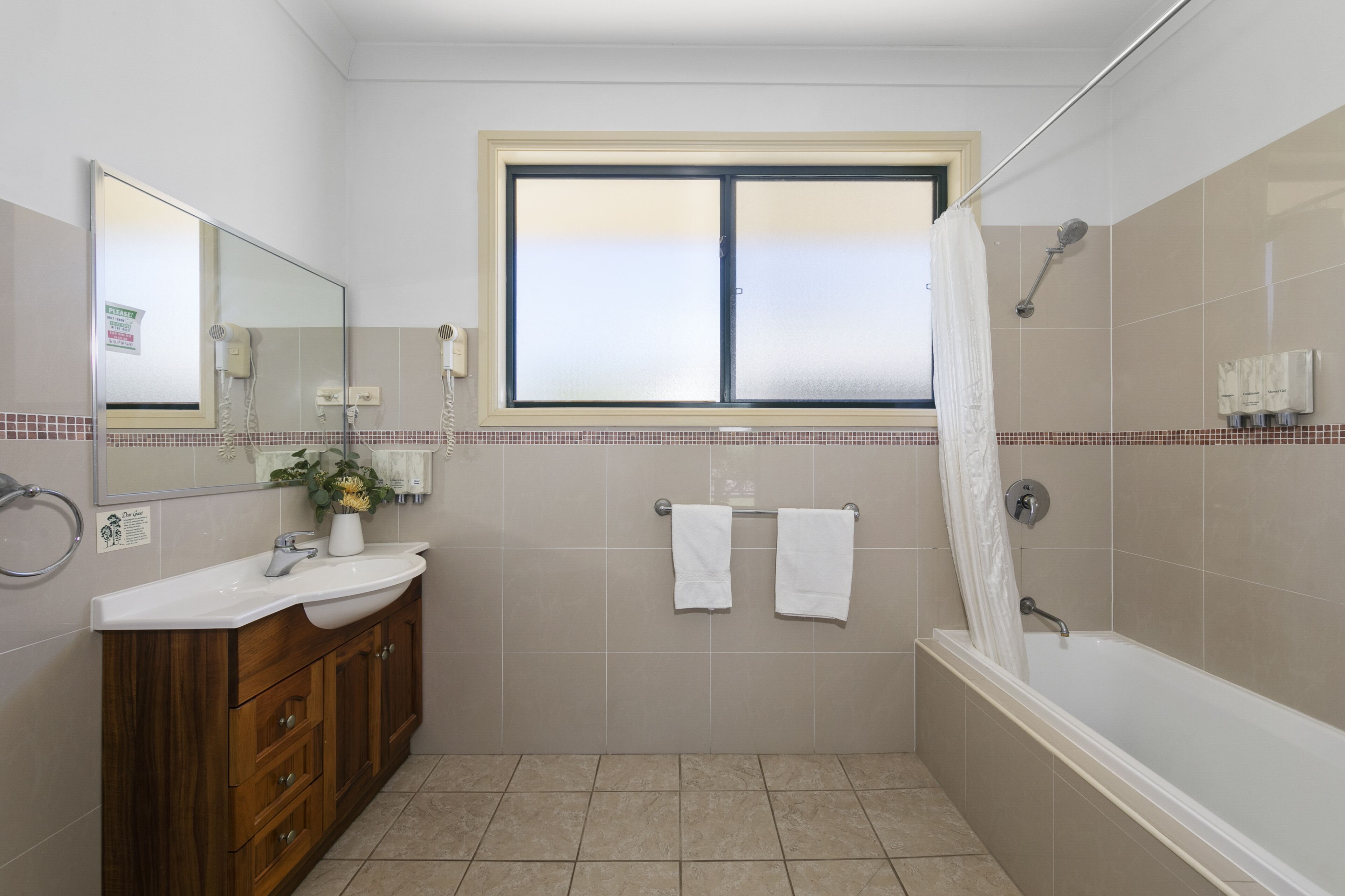 A bathroom with a large window, a bathtub, a vanity with a mirror, and two towels hanging on the wall.