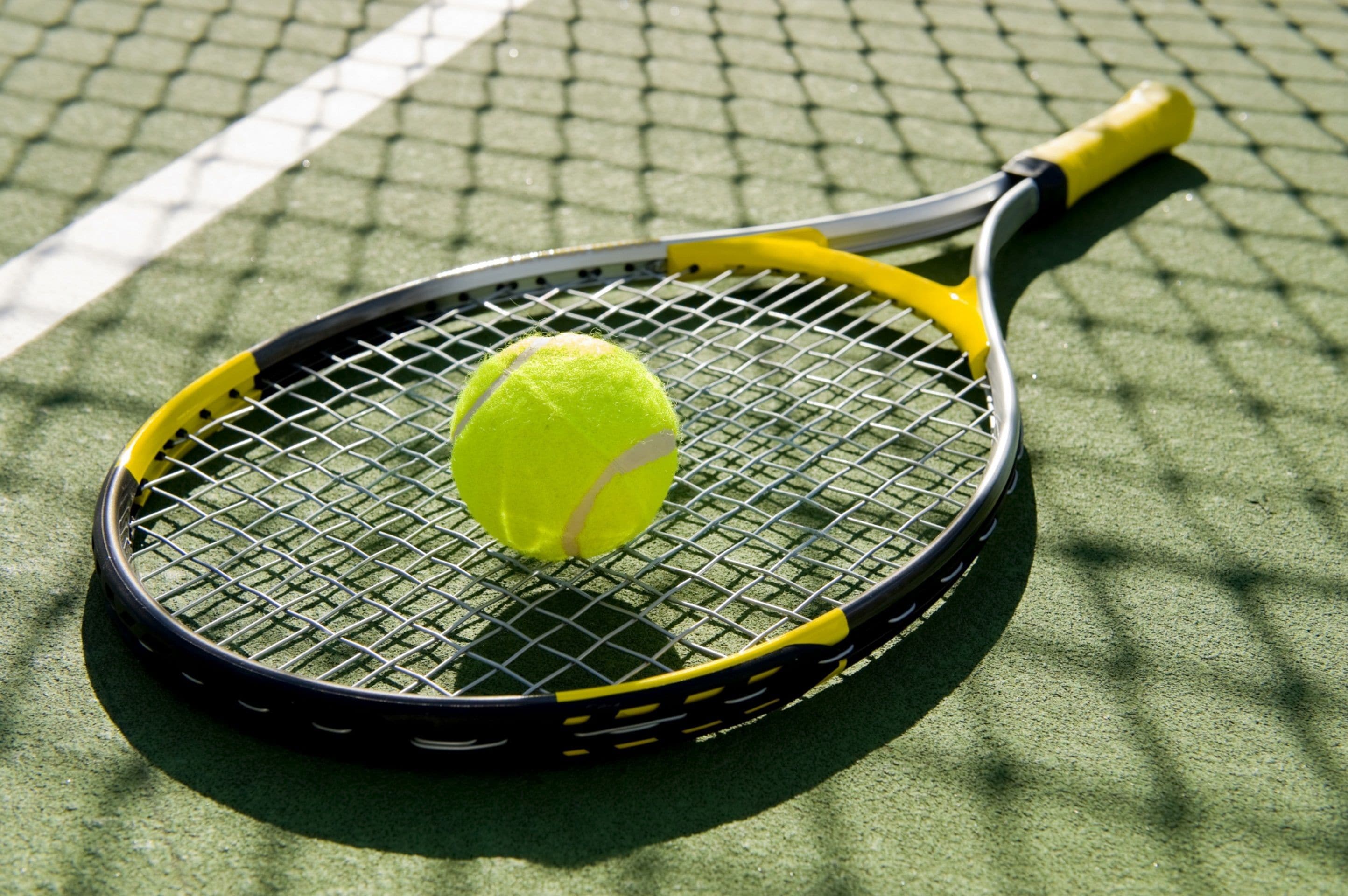 A tennis racket with a yellow handle and a tennis ball on a green court.