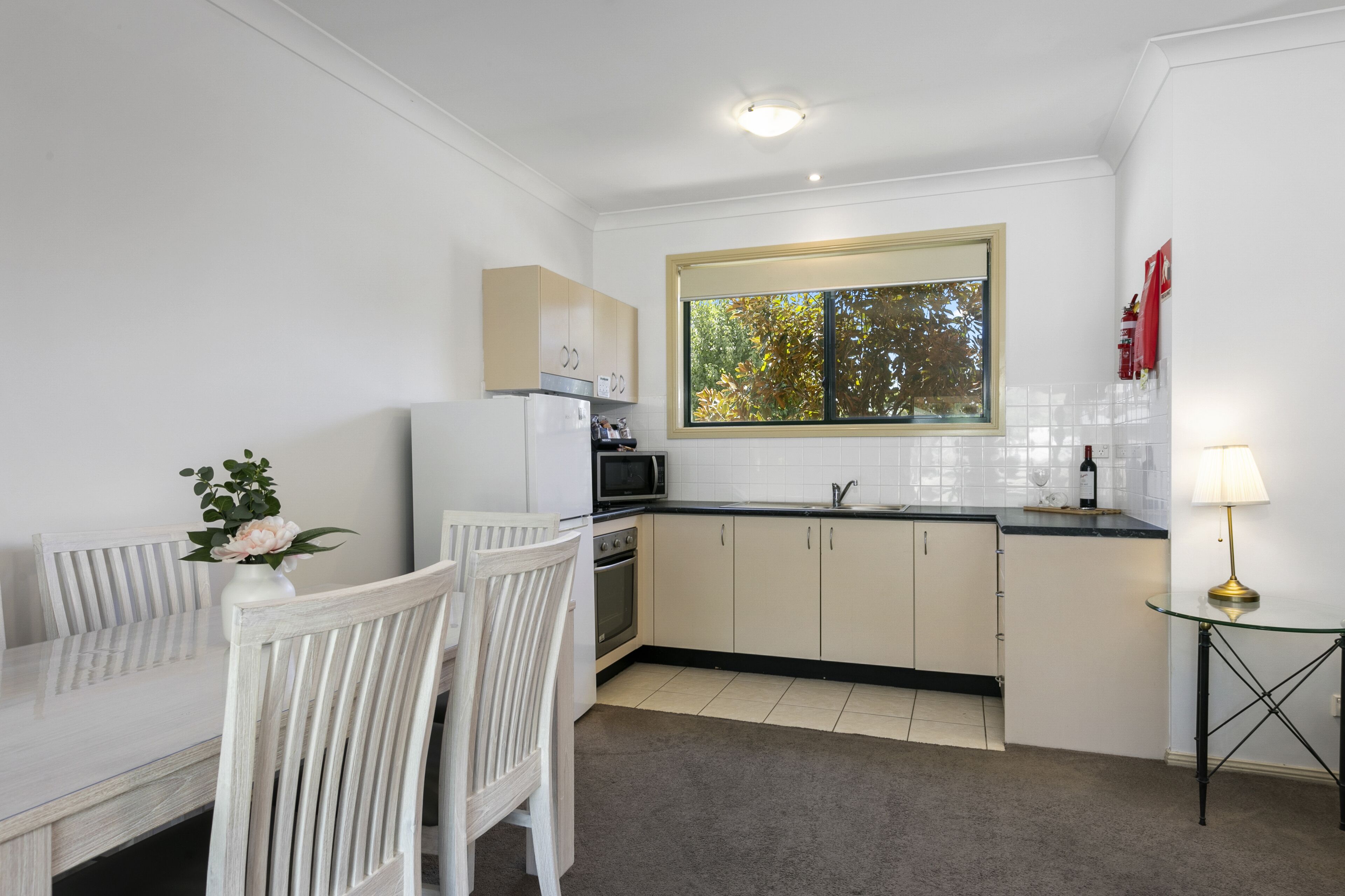 A compact kitchen with white cabinets, a microwave, and a window with a view of trees.