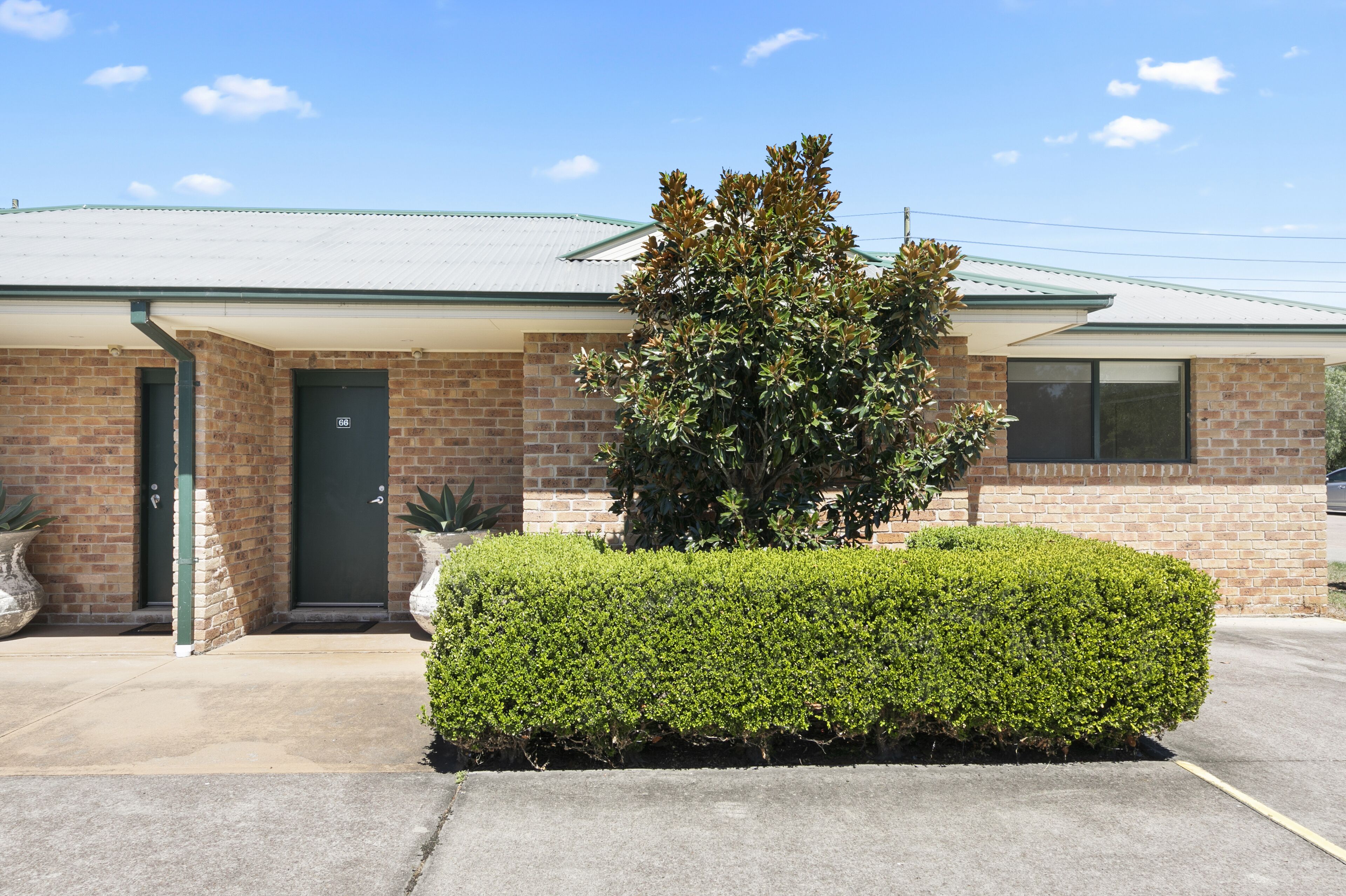 A two-story brick building with a green roof, a front door, and a well-maintained hedge.