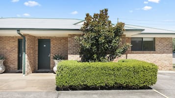 A two-story brick building with a green roof, a front door, and a well-maintained hedge.
