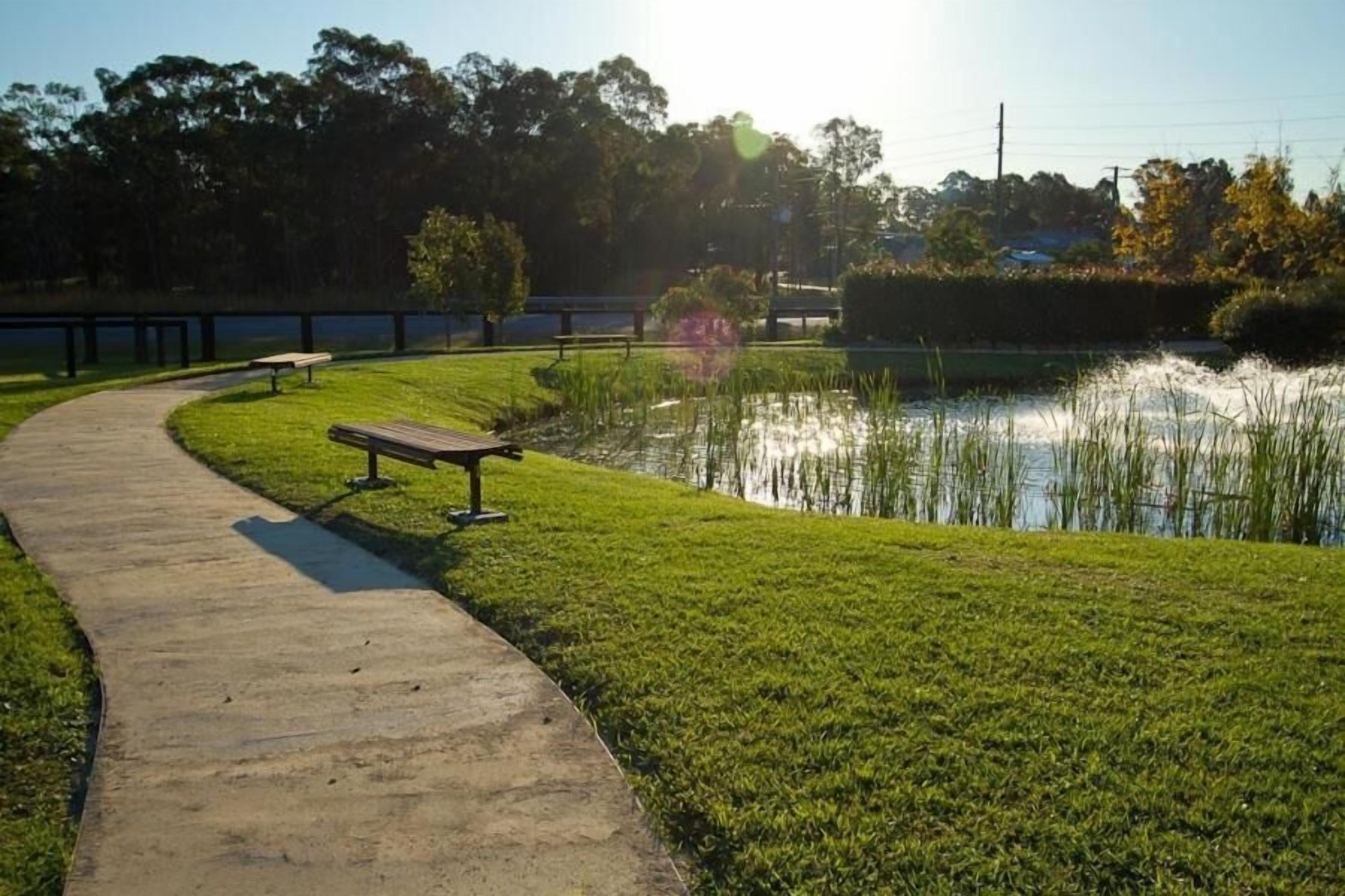 A park with a concrete path, a bench, and a pond.