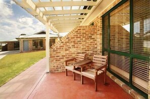 A covered outdoor seating area with a brick wall and a window with blinds.