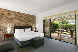 Habitación de hotel moderna con pared de ladrillo, una cama grande, una mesita de noche pequeña, un banco y una puerta corrediza de vidrio que da a un patio exterior.