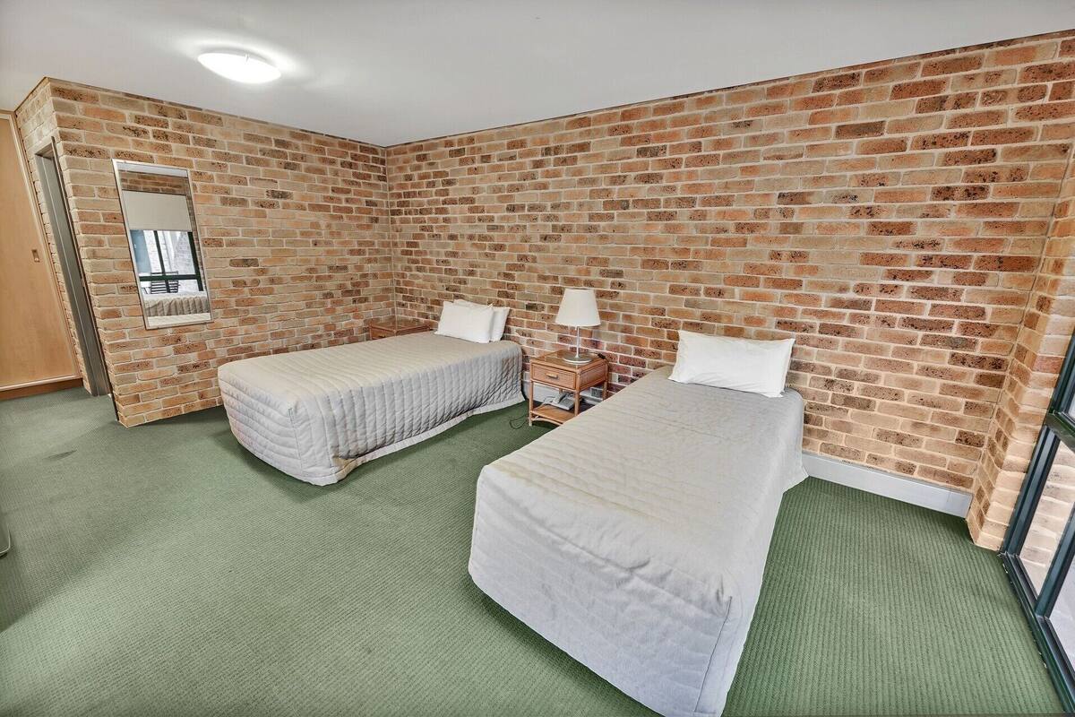 A room with two beds, a mirror, a nightstand, and a brick wall.