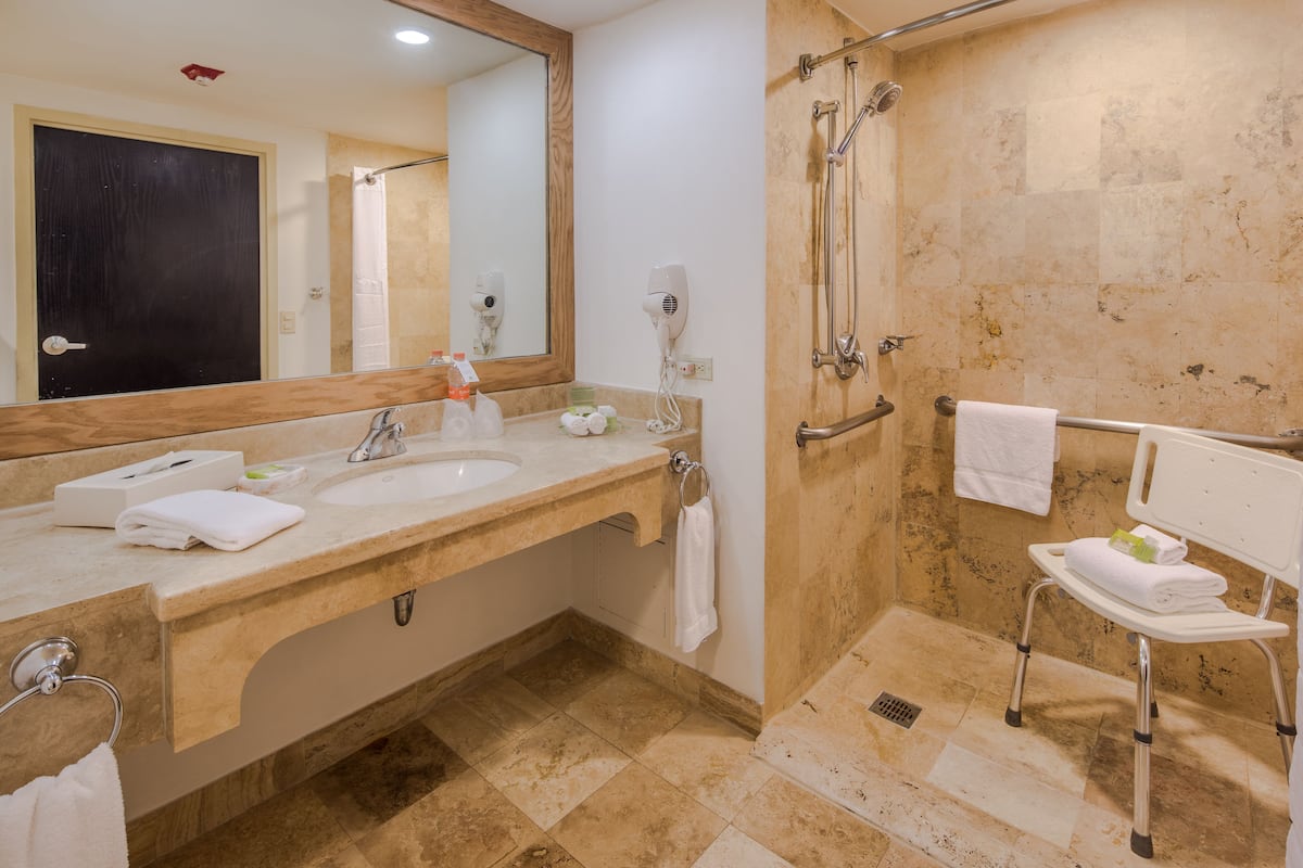 Une salle de bain dotée d’un grand miroir, de deux lavabos, d’une douche et d’un banc accessible aux personnes en fauteuil roulant.