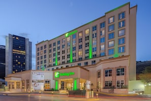 A multi-story Holiday Inn hotel with a prominent green sign, large windows, and a well-lit entrance.