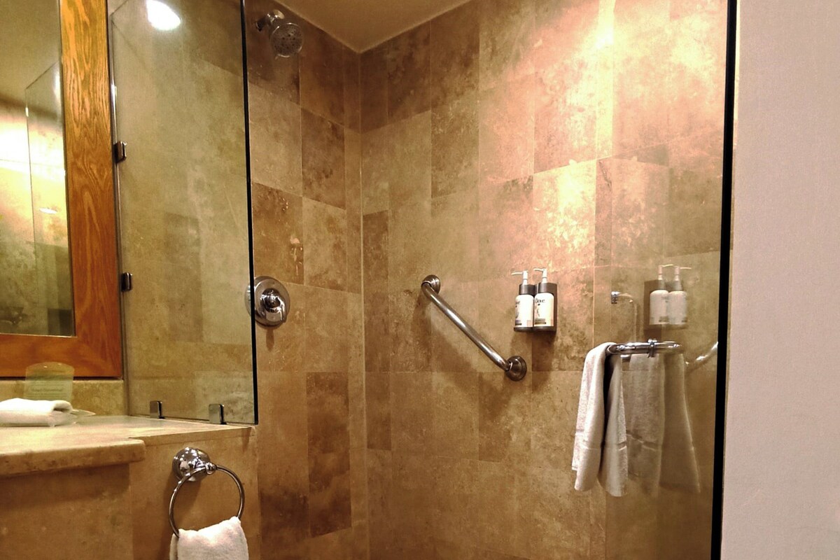 A modern bathroom with a glass shower enclosure, a vanity with a mirror, and toiletries on the wall.