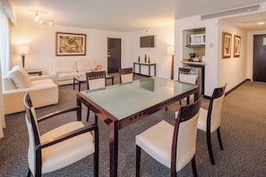 Habitación de hotel con mesa de comedor, sillas, sofá, televisión y kitchenette.