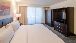 Una habitación de hotel con una cama grande, televisión, armario y ventana con cortinas.