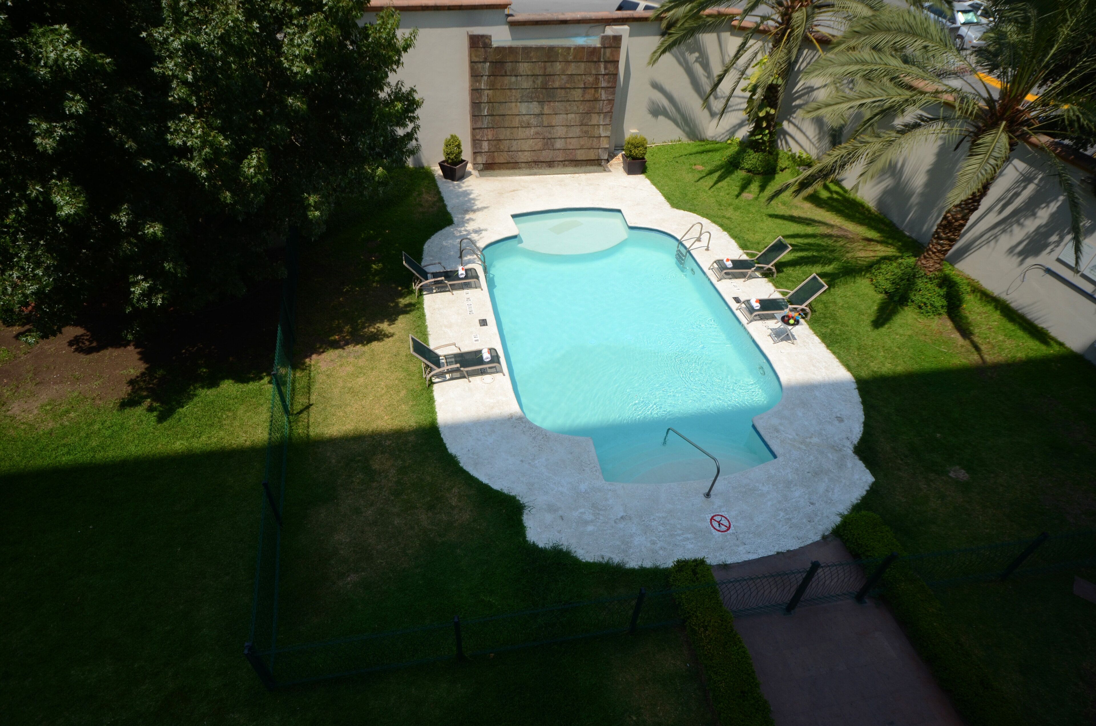 Una piscina rectangular con un deck blanco que la rodea, equipada con múltiples sillas de descanso y una pequeña mesa.