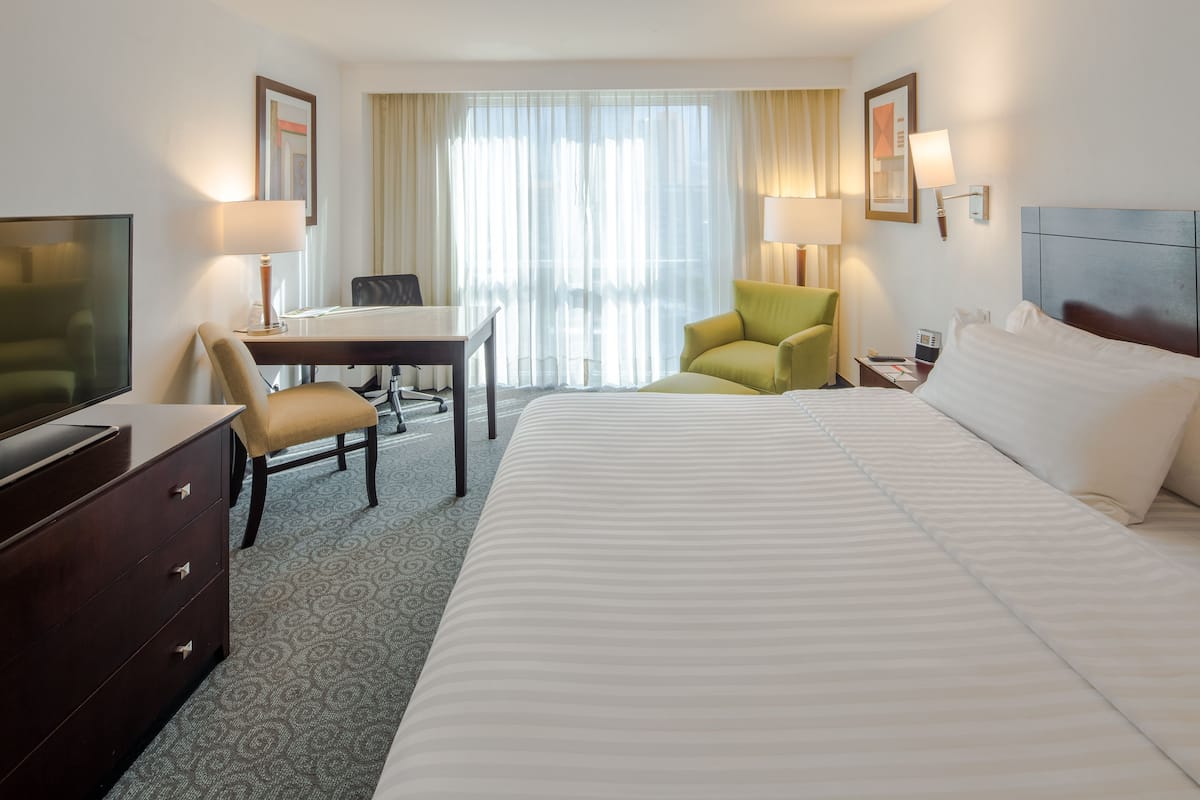Une chambre d’hôtel avec un grand lit, un bureau, une chaise, une télévision et une lampe.