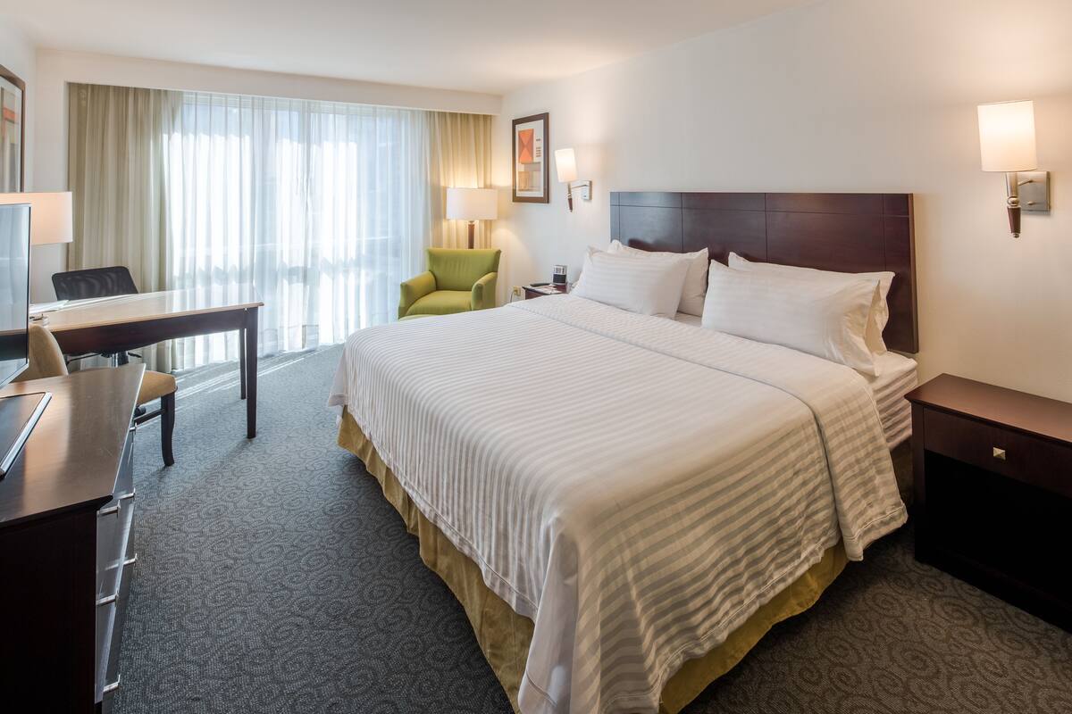 Une chambre d’hôtel avec un grand lit, un bureau, une chaise, une lampe et une table de chevet.
