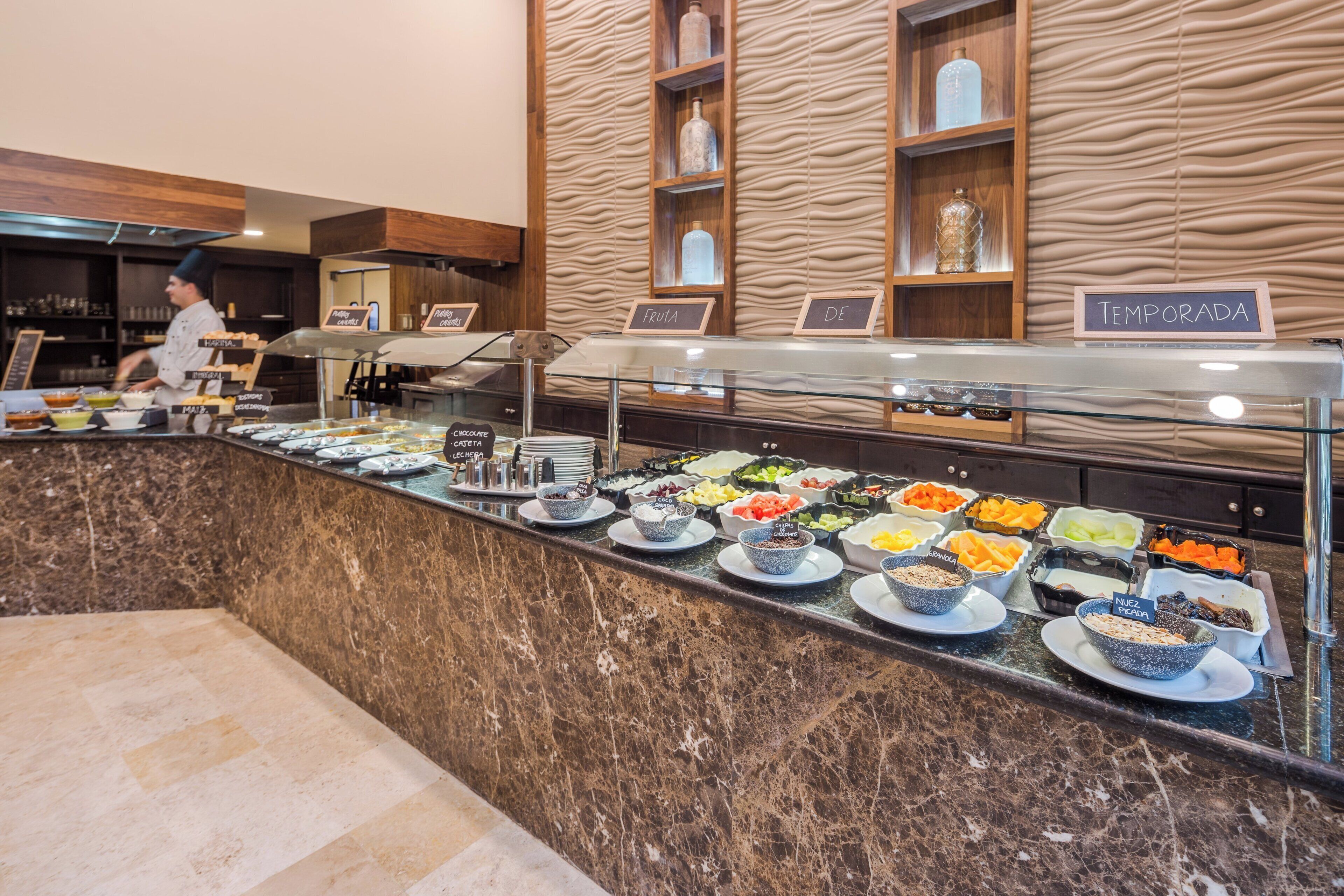 A buffet area with various food stations labeled in Spanish, including 'fruta' and 'leche'.