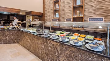 Zona de buffet con distintas estaciones de comida identificadas en español, incluyendo 'fruta' y 'leche'.
