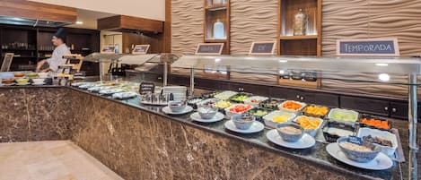 Un espace buffet avec différents stands de nourriture, dont les noms sont indiqués en espagnol, notamment « fruta » et « leche ».