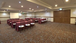 Un salón de conferencias con filas de mesas y sillas, una pantalla para proyector y una puerta grande de madera.