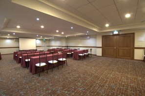 A conference room with rows of tables and chairs, a projector screen, and a large wooden door. - Holiday Inn Monterrey Valle by IHG (San Pedro Garza García)