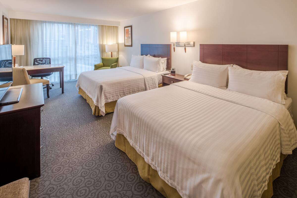 Une chambre d’hôtel avec deux lits, un bureau, une chaise, une télévision et une fenêtre avec des rideaux.