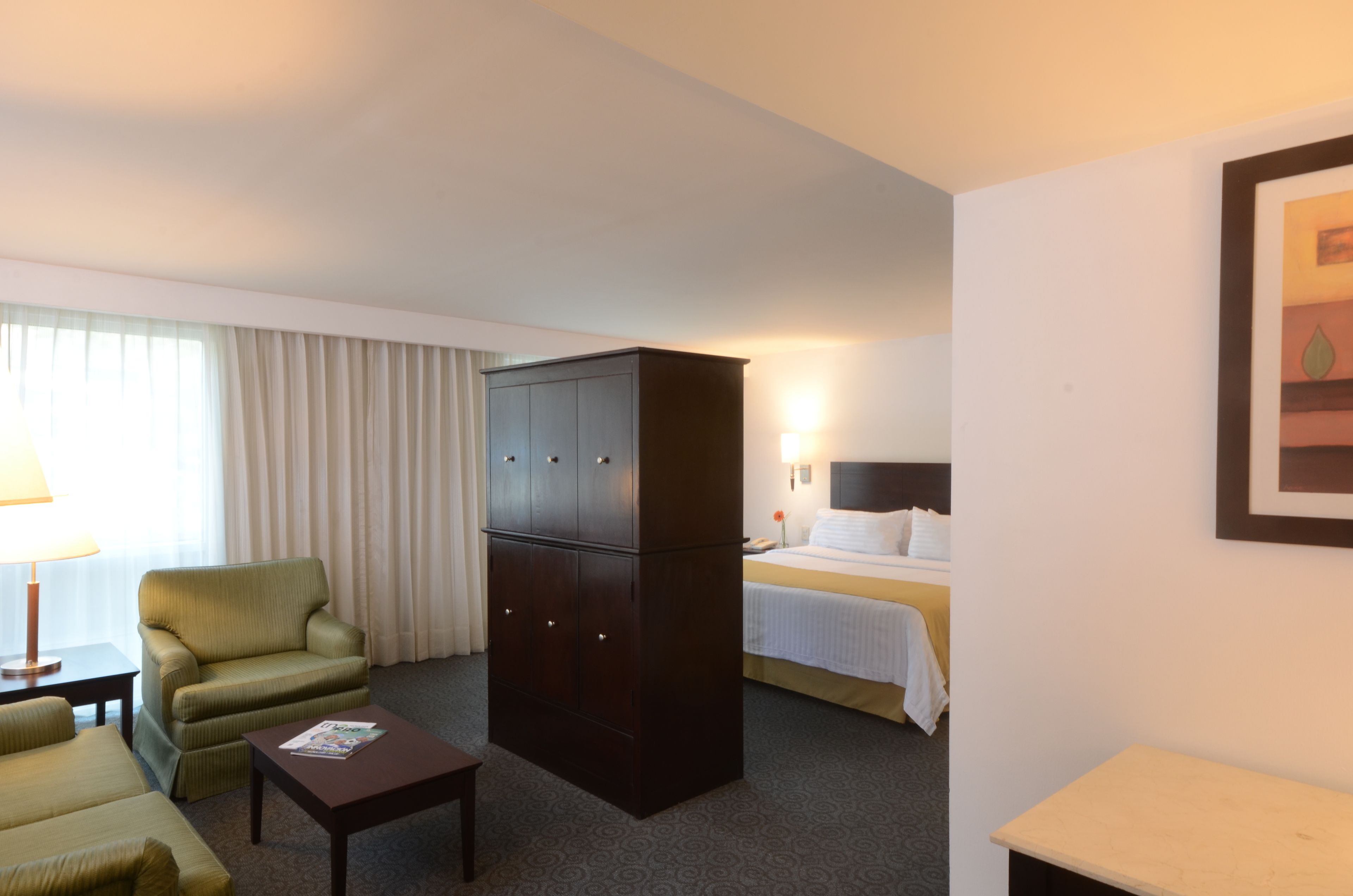 Een hotelkamer met een bed, een bureau, een stoel, een kast en een lamp.