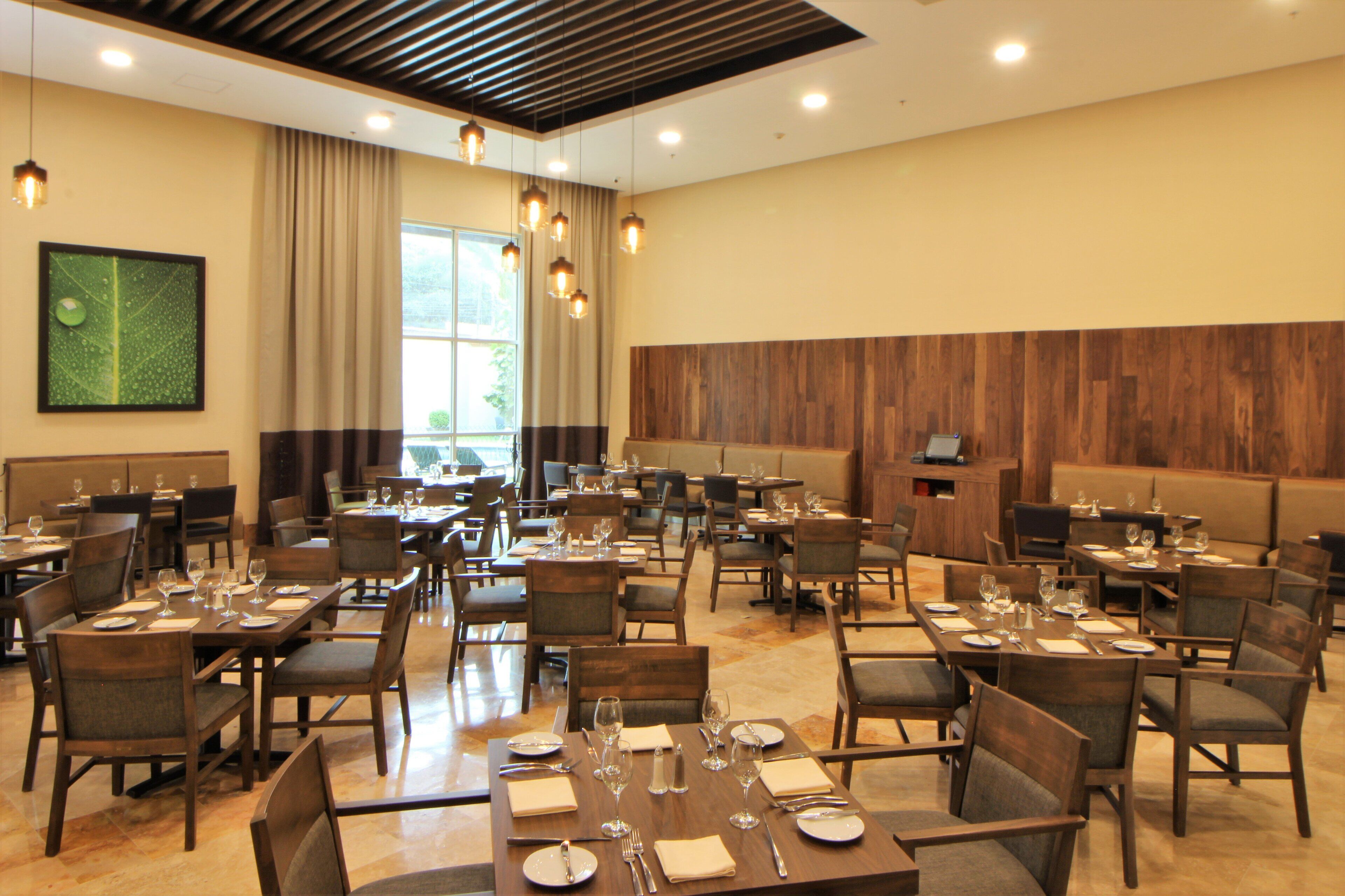 Une salle à manger d’hôtel avec de nombreuses tables et chaises, de grandes fenêtres et un mur en bois.