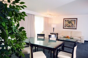 Habitación de hotel con mesa de comedor de vidrio, dos sillas, un sofá, una lámpara y un cuadro en la pared.