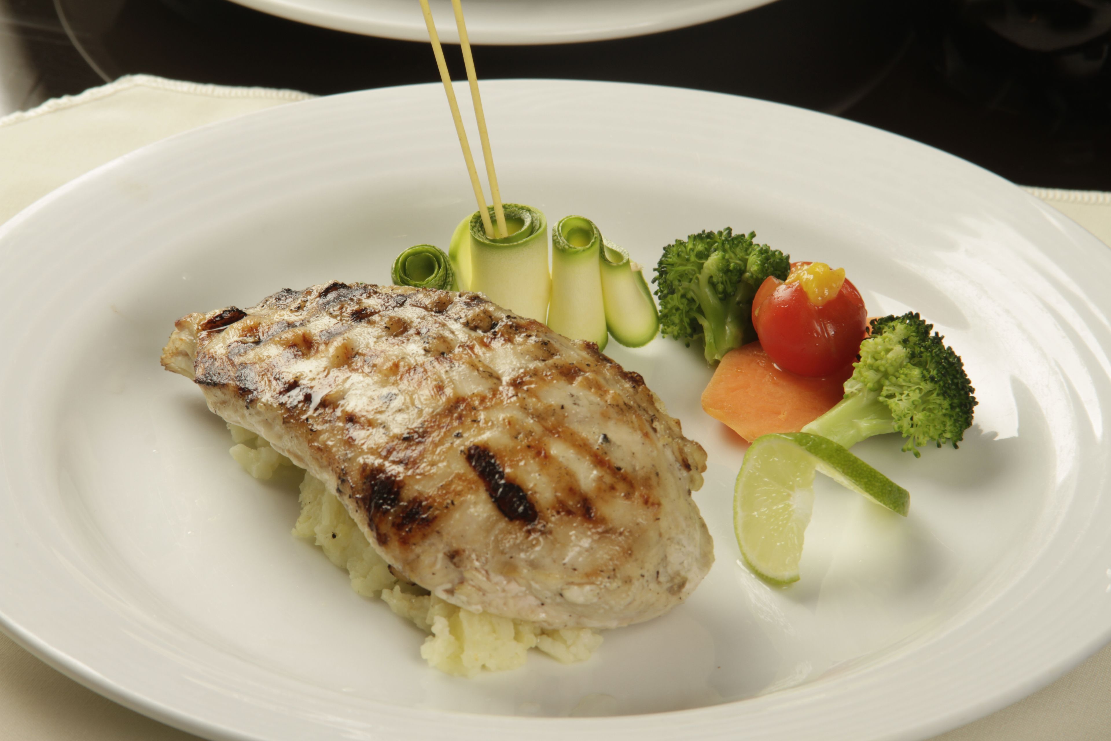 A plate with grilled chicken, broccoli, carrots, and a lime wedge.