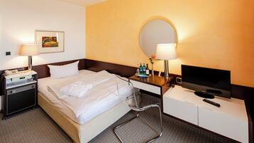 A hotel room with a bed, bedside table, TV, and a small desk with a mirror.