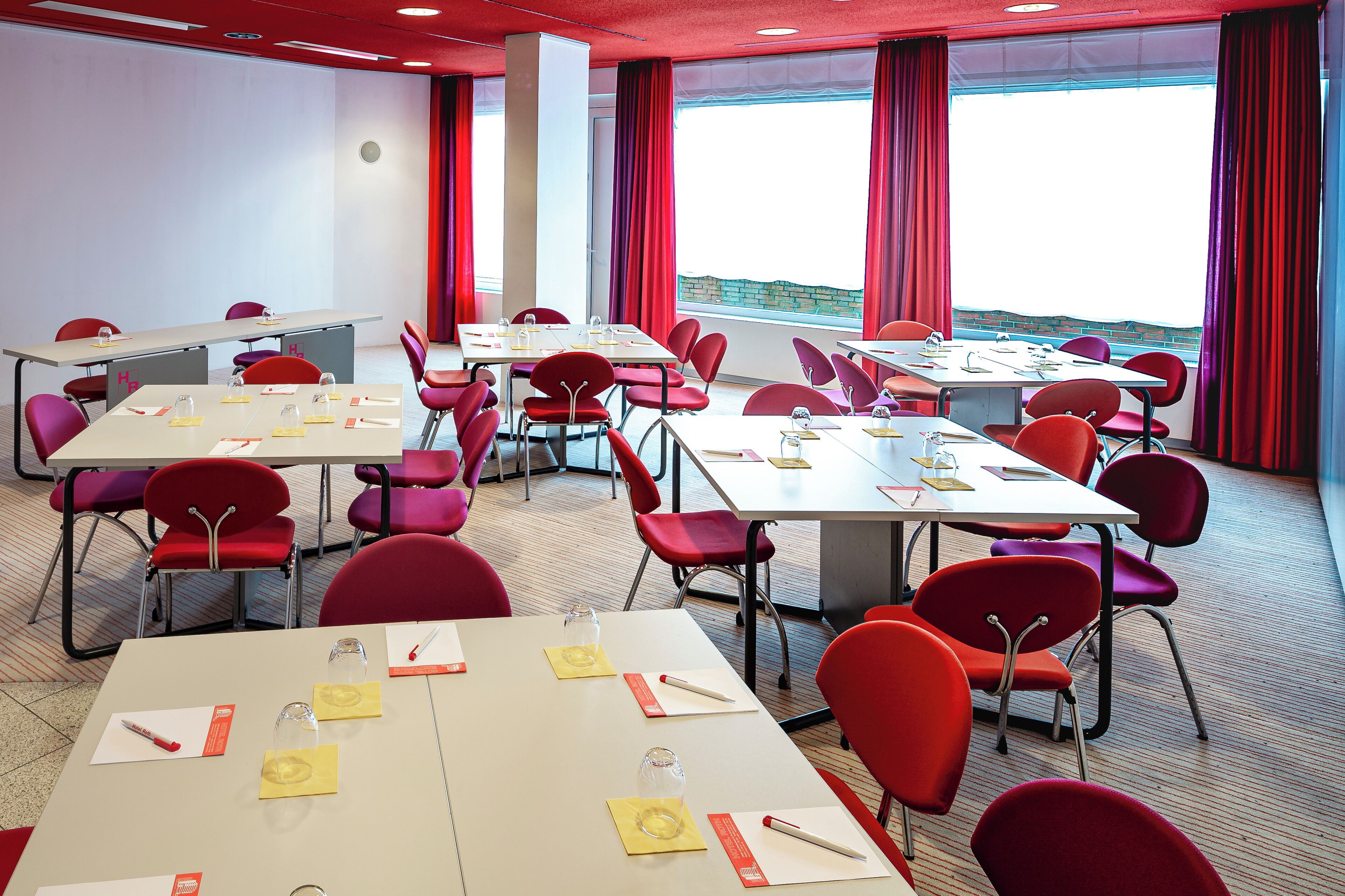 Ein Konferenzraum mit Tischen, Stühlen und einem großen Fenster mit Vorhängen.